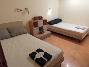 Un dormitorio con dos camas, un aparador de madera, una mesita de noche y una lámpara fijada a la pared.