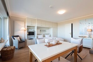 Una cocina moderna y luminosa con armarios blancos, una mesa de comedor y una zona de estar acogedora con muebles de mimbre.