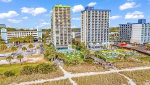 Un hôtel de grande hauteur, avec de nombreux étages, un parking et une piscine équipée de chaises longues.