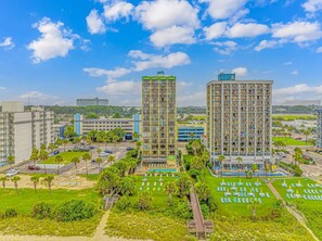 A high-rise hotel with multiple floors, a swimming pool, and a well-maintained lawn with sun loungers.