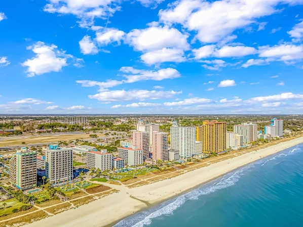 A coastal cityscape with high-rise buildings, a beach, and a clear sky.