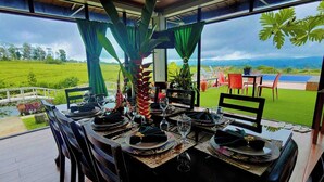 Un comedor con una mesa preparada para cuatro personas, con vistas a un paisaje exuberante y al mar y las montañas.