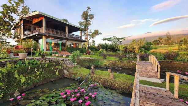 Una casa moderna con un balcón grande que da a un jardín con un estanque y flores rosas.