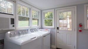 A laundry room with a front-loading washer and dryer, large windows, and a door with a fire extinguisher. - Countryside Retreat (Soddy-Daisy)