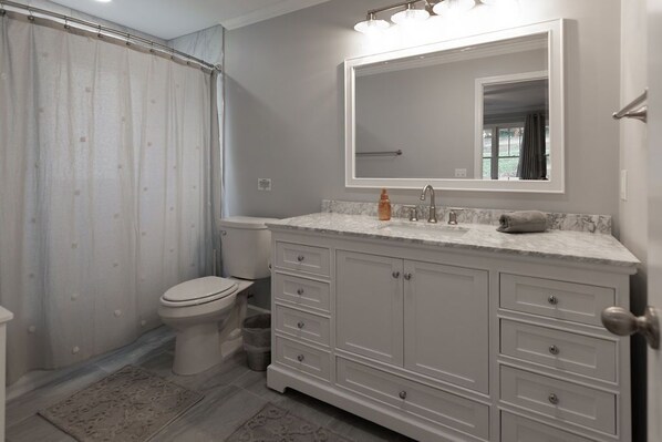 A bathroom with a toilet, a shower curtain, a sink with a mirror, and a cabinet. - Countryside Retreat (Soddy-Daisy)