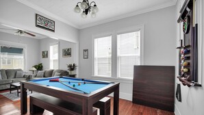 Una sala de billar con mesa de pool, un sofá y un soporte para billares.