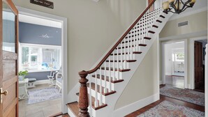 Una escalera con balaustres de madera y un candelabro, que conduce a una habitación con un letrero que dice 'Relax' y vistas al exterior.
