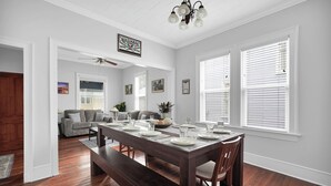 Comedor con mesa de madera dispuesta para cuatro personas, un banco y un sofá en la sala de estar contigua.