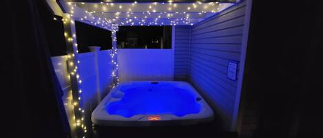 Een hottub met blauwe verlichting, omringd door lichtslingers, in een overdekte buitenruimte.