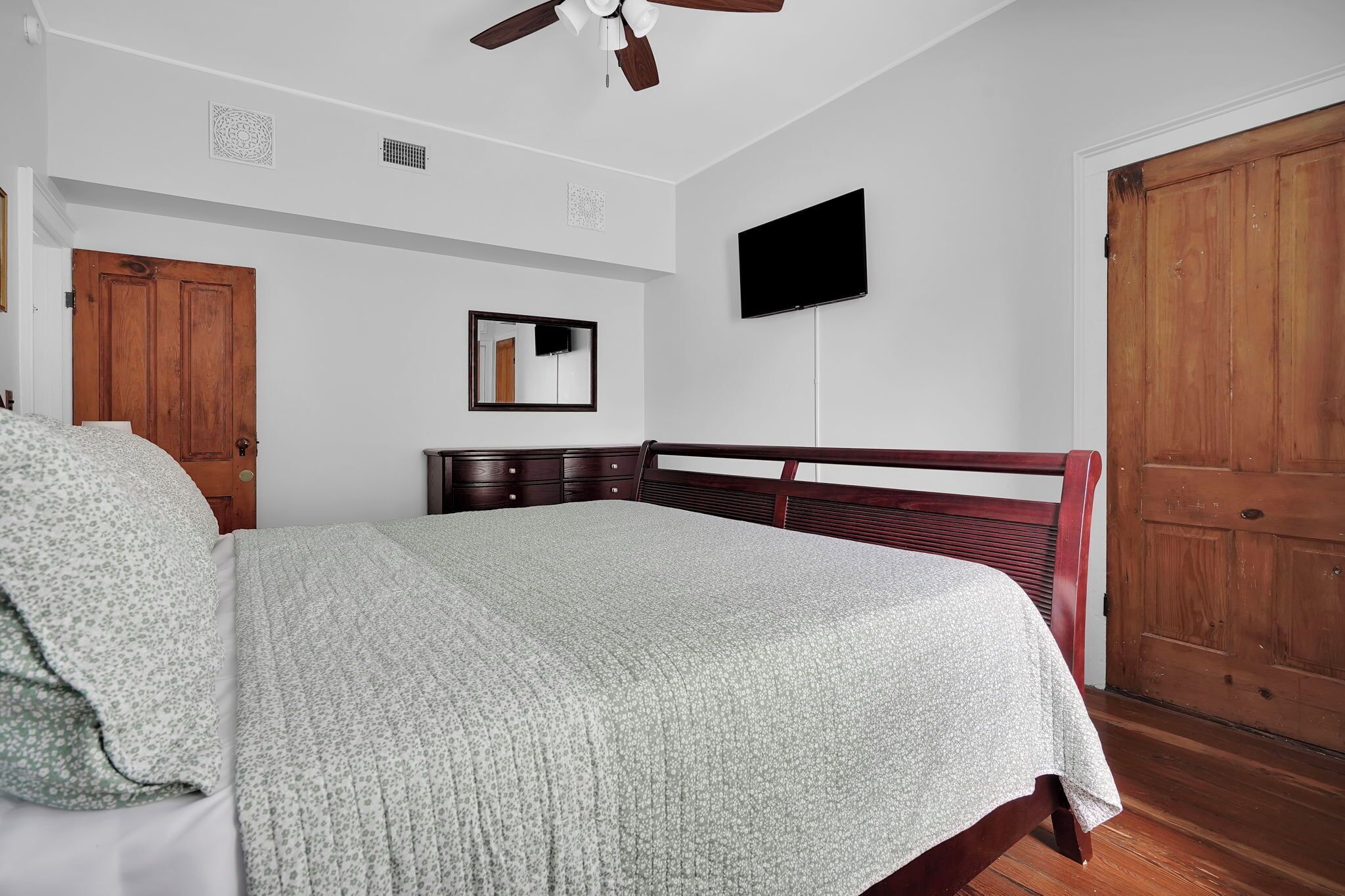 Une chambre à coucher comprenant un lit, une armoire en bois, un ventilateur de plafond, un téléviseur à écran plat et un miroir.