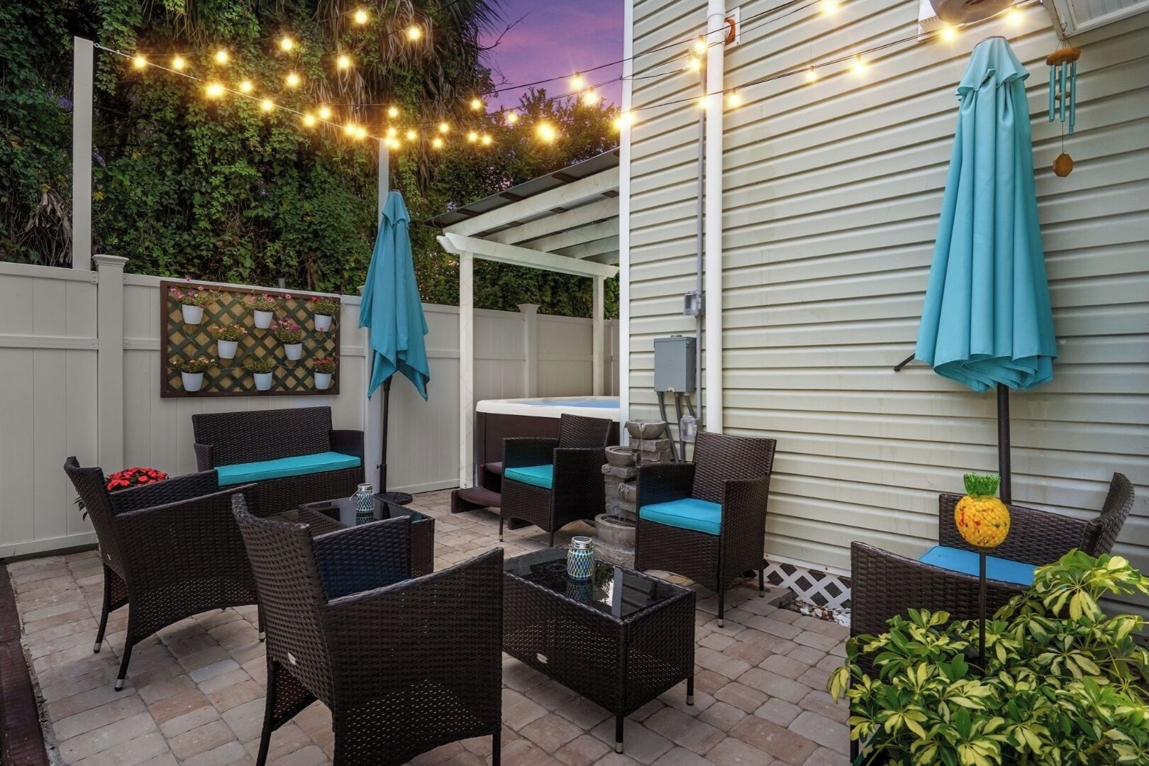 An outdoor patio with wicker furniture, a hot tub, string lights, and a decorative pineapple.