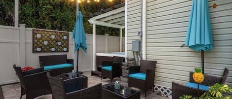 An outdoor patio with wicker furniture, a hot tub, string lights, and a decorative pineapple.