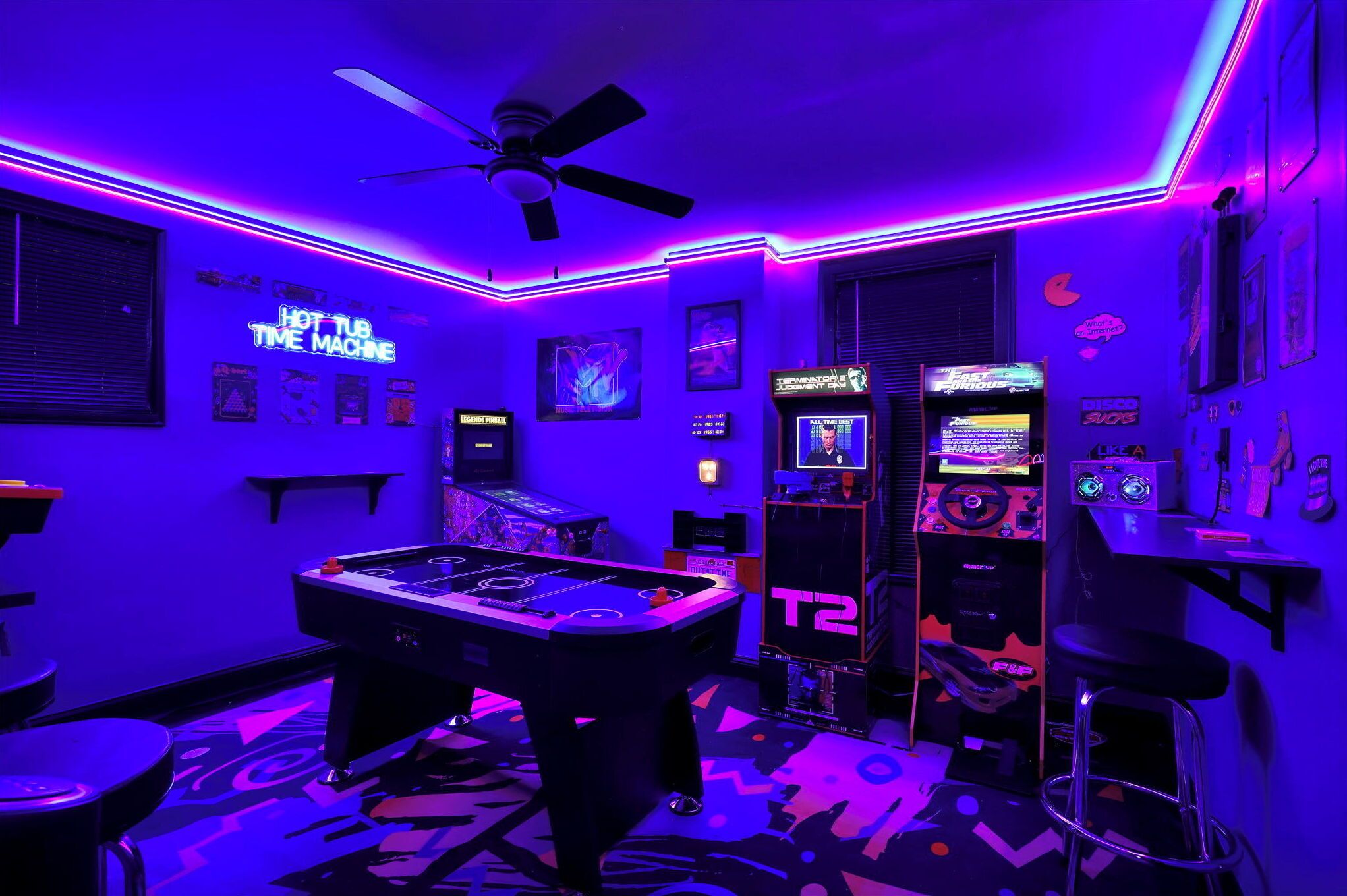 A room with a pool table, arcade machines, and neon lighting.