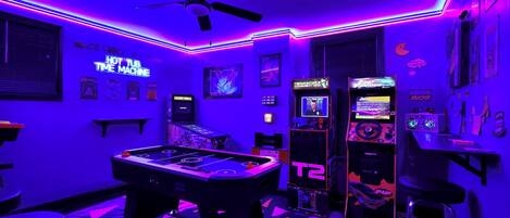 A room with a pool table, arcade machines, and neon lighting.