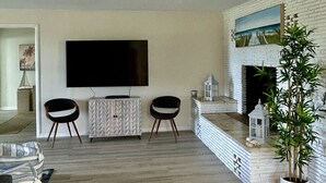 Ein Wohnzimmer mit Flachbildfernseher, zwei Stühlen, einem weißen Kamin und einer Topfpflanze.