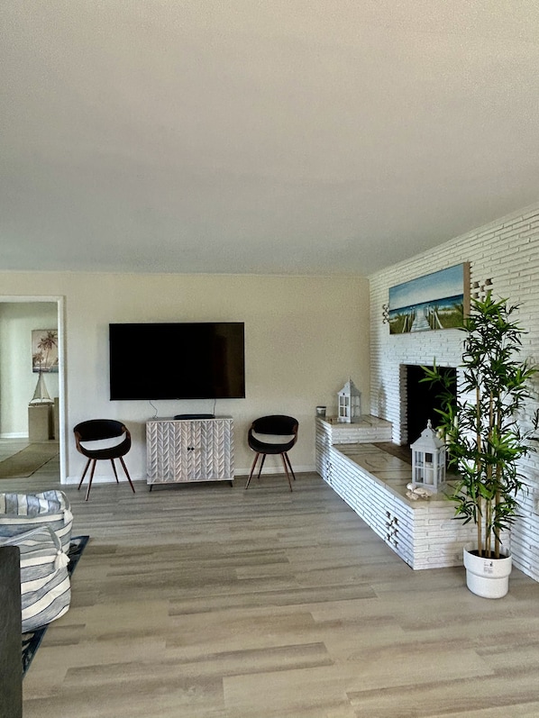 Una sala de estar con una televisión de pantalla plana, dos sillones, una chimenea blanca y una planta en maceta.