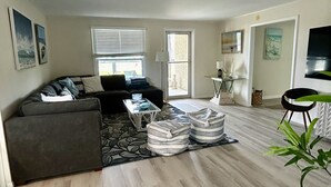Ein modernes Wohnzimmer mit einer Couch, Hocker, einem Couchtisch und einem Fernseher.