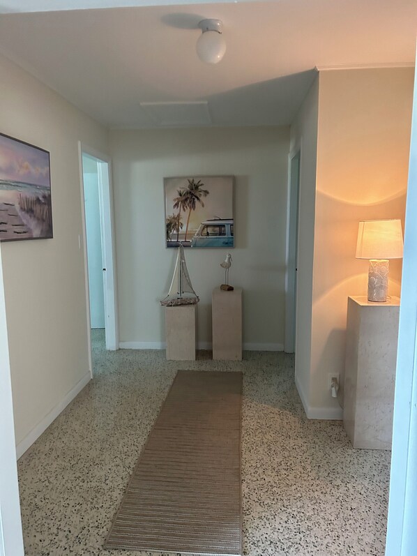 A hallway with a speckled floor, a wooden bench, a hanging birdcage, a framed picture, and a lamp. - Ocean Breeze Home (Summerland Key)