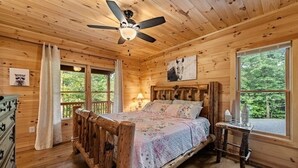 Un dormitorio tipo cabaña de madera con una cama, un ventilador de techo, una ventana y un aparador.