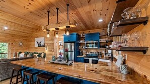 Un interior de madera con una zona de bar central, armarios azules y un refrigerador de acero inoxidable.