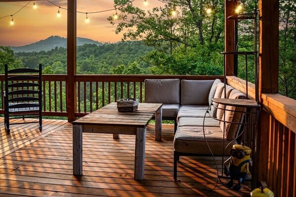 Une terrasse en bois avec un canapé et un fauteuil, une table et des guirlandes lumineuses.