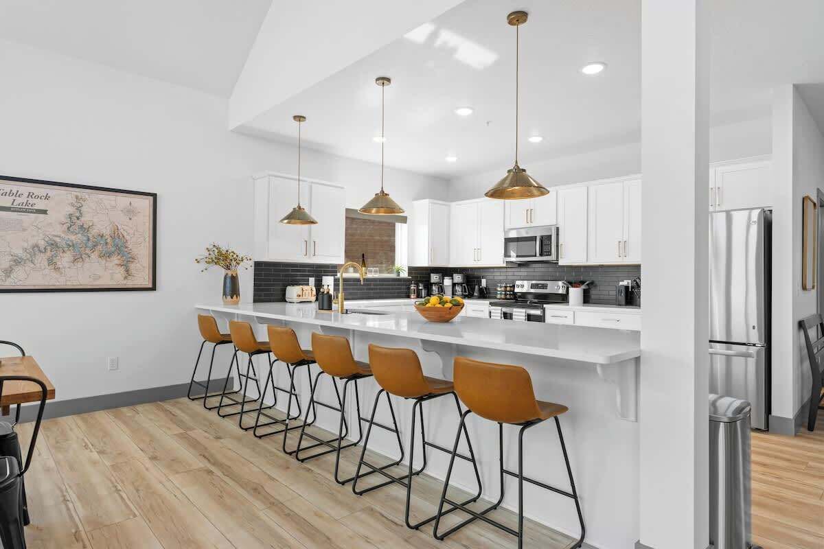 A modern kitchen with white cabinets, a central island with bar stools, stainless steel appliances, and pendant lighting.