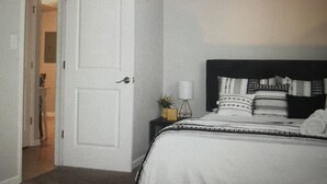 A bedroom with a bed, a nightstand, and a door leading to another room.