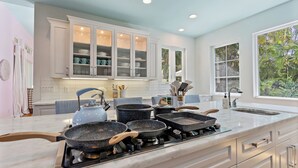 A kitchen with white cabinets, a large island with a sink, and a view of greenery outside. - Sapphire Shores | Luxury Pool, 2 Fireplaces, Game Room + 2 Bars! (Sarasota)