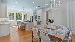 A modern kitchen with white cabinetry, a central island, and a dining area set for six with white tableware. - Sapphire Shores | Luxury Pool, 2 Fireplaces, Game Room + 2 Bars! (Sarasota)