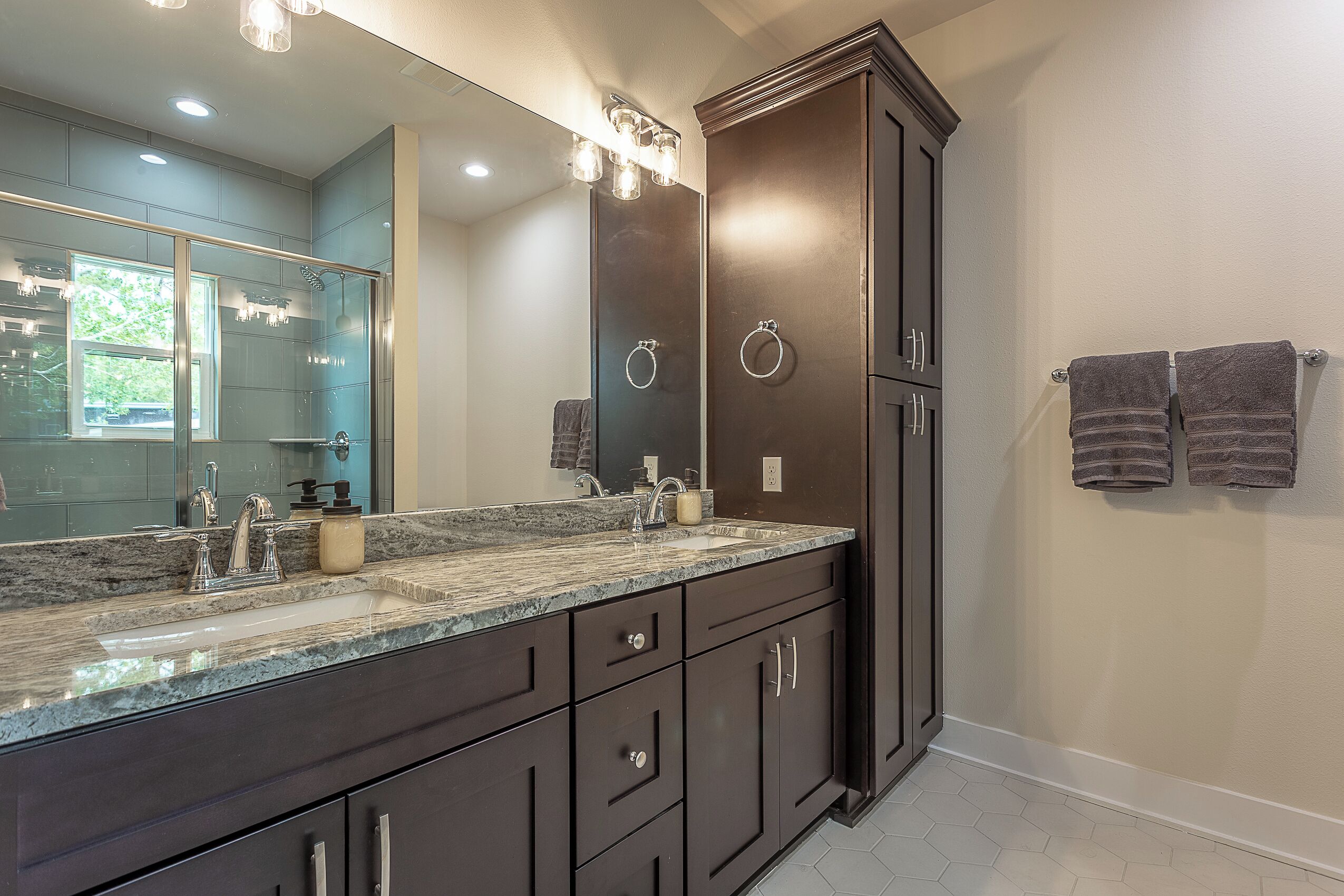 Un baño moderno con tocador de madera oscura, un espejo grande y encimera de granito.
