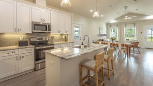 Una cocina amplia con armarios blancos, electrodomésticos de acero inoxidable y una isla grande con taburetes de bar.