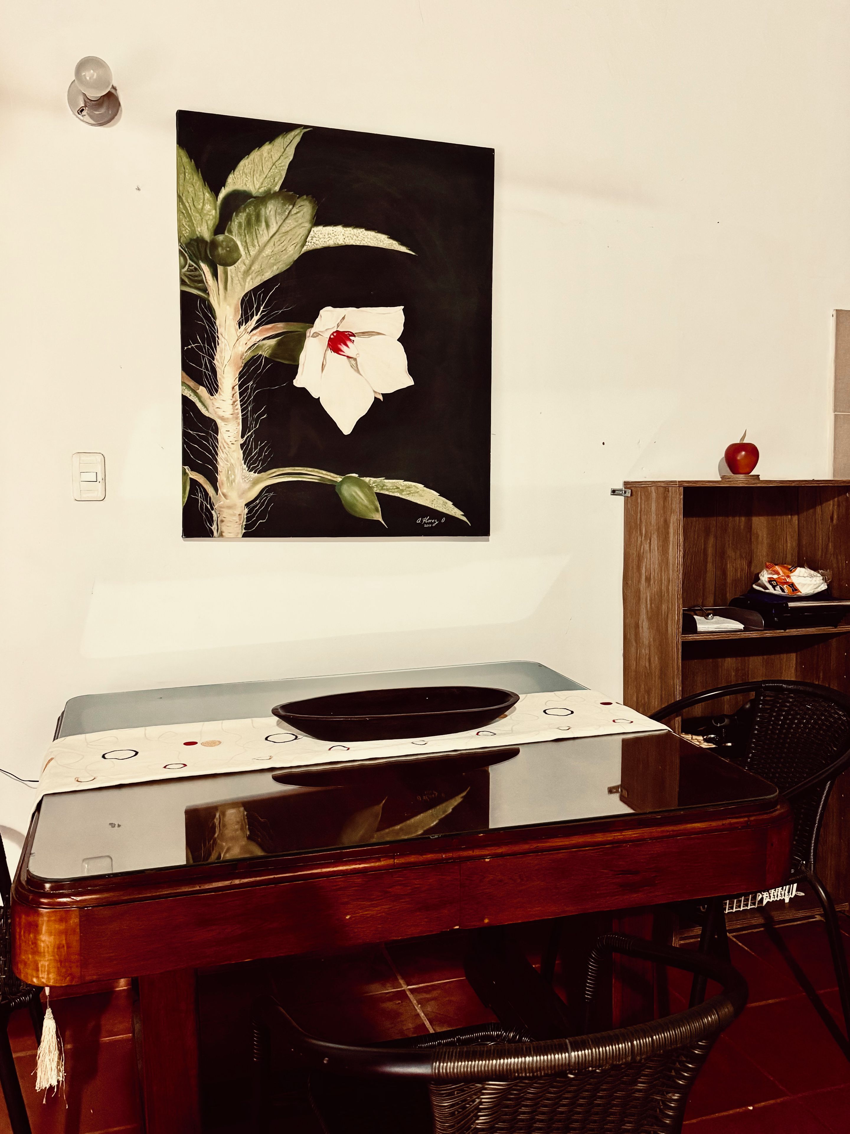 Een eethoek met een tafel, stoelen, een schilderij aan de muur en een houten kastje met een appel erbovenop.