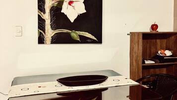 Een eethoek met een tafel, stoelen, een schilderij aan de muur en een houten kastje met een appel erbovenop.