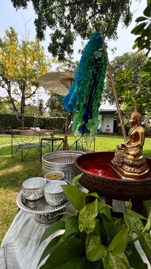 A garden setting with a Buddha statue, a decorative umbrella, and a table with dishes. - UDEE Cozy Hotel (Chiang Mai)