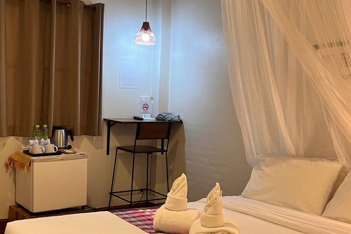 Ein Hotelzimmer mit Bett, Schreibtisch, Stuhl, Nachttisch, einer Kaffeemaschine und einer Wasserflasche.