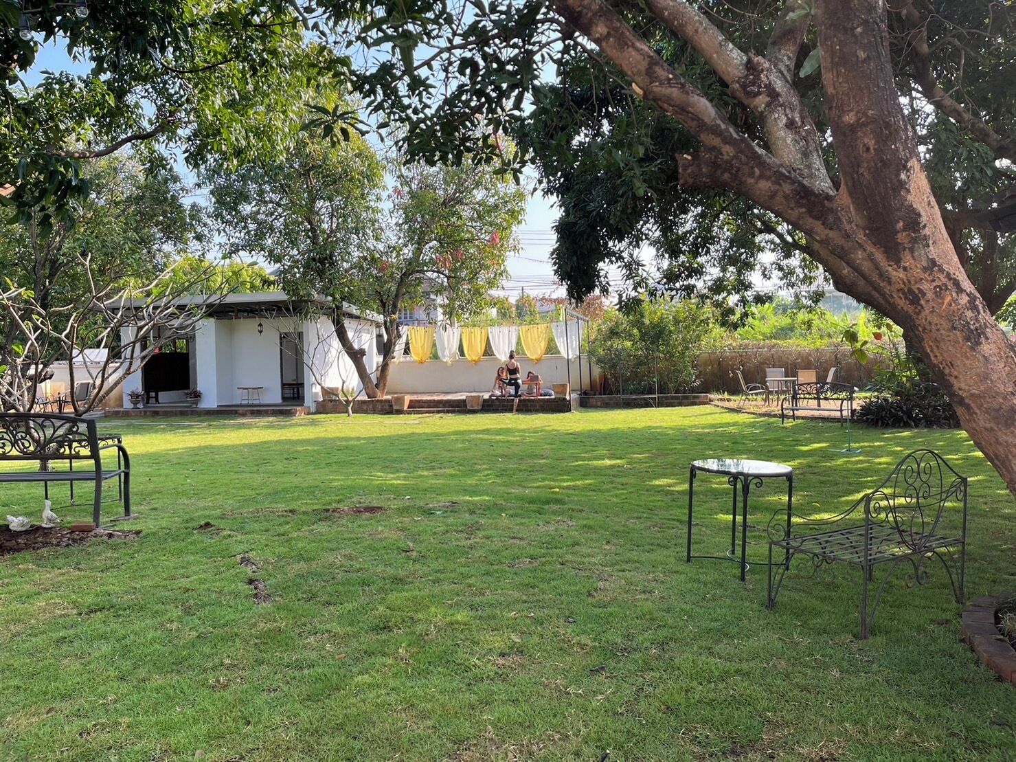 A grassy outdoor area with a white building, a covered seating area, and metal furniture.