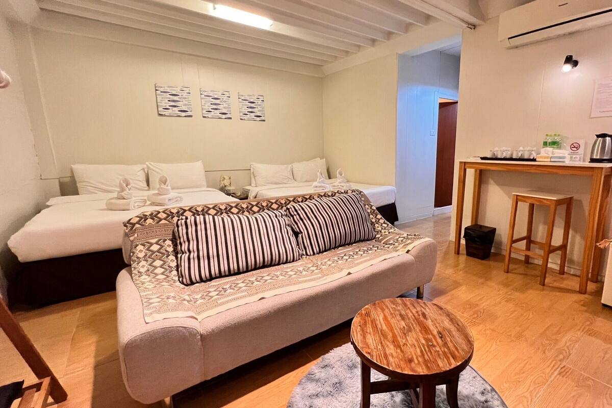 Ein gemütliches Zimmer mit zwei Betten, einem Schlafsofa, einem kleinen Holztisch und einem Kühlschrank.