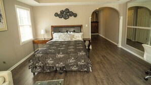 A bedroom with a large bed, a nightstand, a lamp, and a wall art piece. - Nice and Cousy guest suite (Roswell)