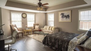 A spacious bedroom with a large bed, a ceiling fan, a desk, and a chair. There are two windows with blinds, a clock on the wall, and a framed picture. - Nice and Cousy guest suite (Roswell)