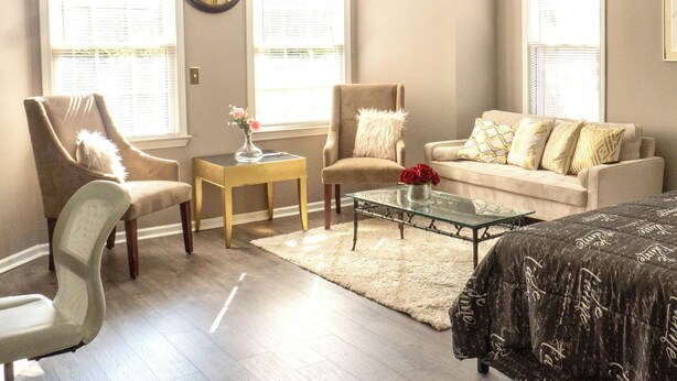 A living room with a ceiling fan, two windows with blinds, a sofa, a chair, a coffee table, and a clock on the wall. - Nice and Cousy guest suite (Roswell)
