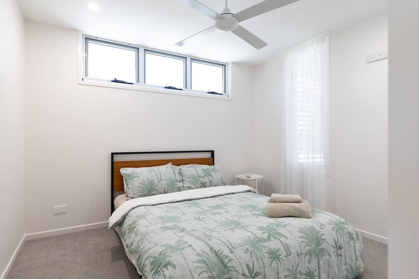 A bedroom with a bed, a ceiling fan, a window, and a nightstand.