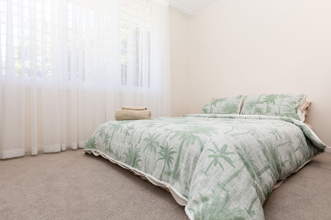 A bedroom with a bed, a window with sheer curtains, and a carpeted floor.
