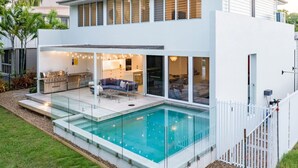 Ein modernes Haus mit Schwimmbad, Außenküche und einer überdachten Terrasse.