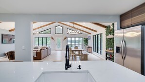 Une cuisine moderne dotée d’un grand îlot central, de poutres en bois et donnant sur un espace repas.