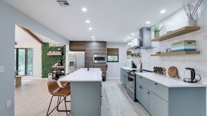 Une cuisine moderne dotée d’un îlot central, d’appareils électroménagers intégrés et d’un mur végétal agrémenté d’une enseigne indiquant « Café ».