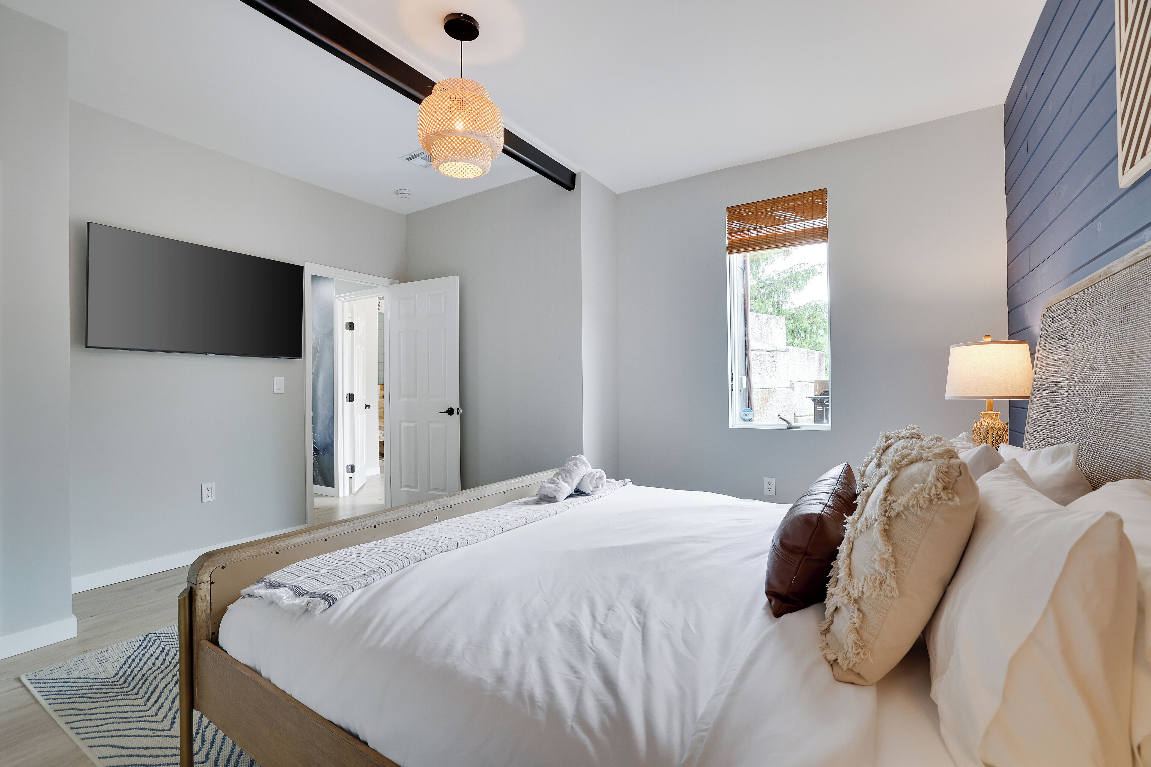 A bedroom with a bed, a television mounted on the wall, a window with blinds, and a bedside lamp.