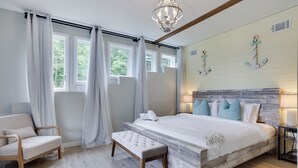 Une chambre à coucher avec une tête de lit en bois, un grand lit, un banc, une chaise et une fenêtre avec des rideaux.