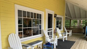 A covered porch with white Adirondack chairs and a bench, yellow walls, and large windows. - Classic Seaman's Lodge - directly across from the Quarterdeck (Pet Friendly!) (Summerville Center)