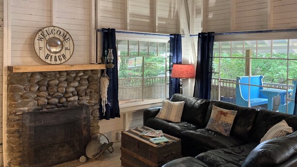 A cozy room with a stone fireplace, a leather sofa, and a view of the outdoors through large windows. - Classic Seaman's Lodge - directly across from the Quarterdeck (Pet Friendly!) (Summerville Center)