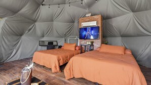 Ein Zeltraum mit zwei Betten, einem Fernseher und einem Tisch mit einem Getränk.